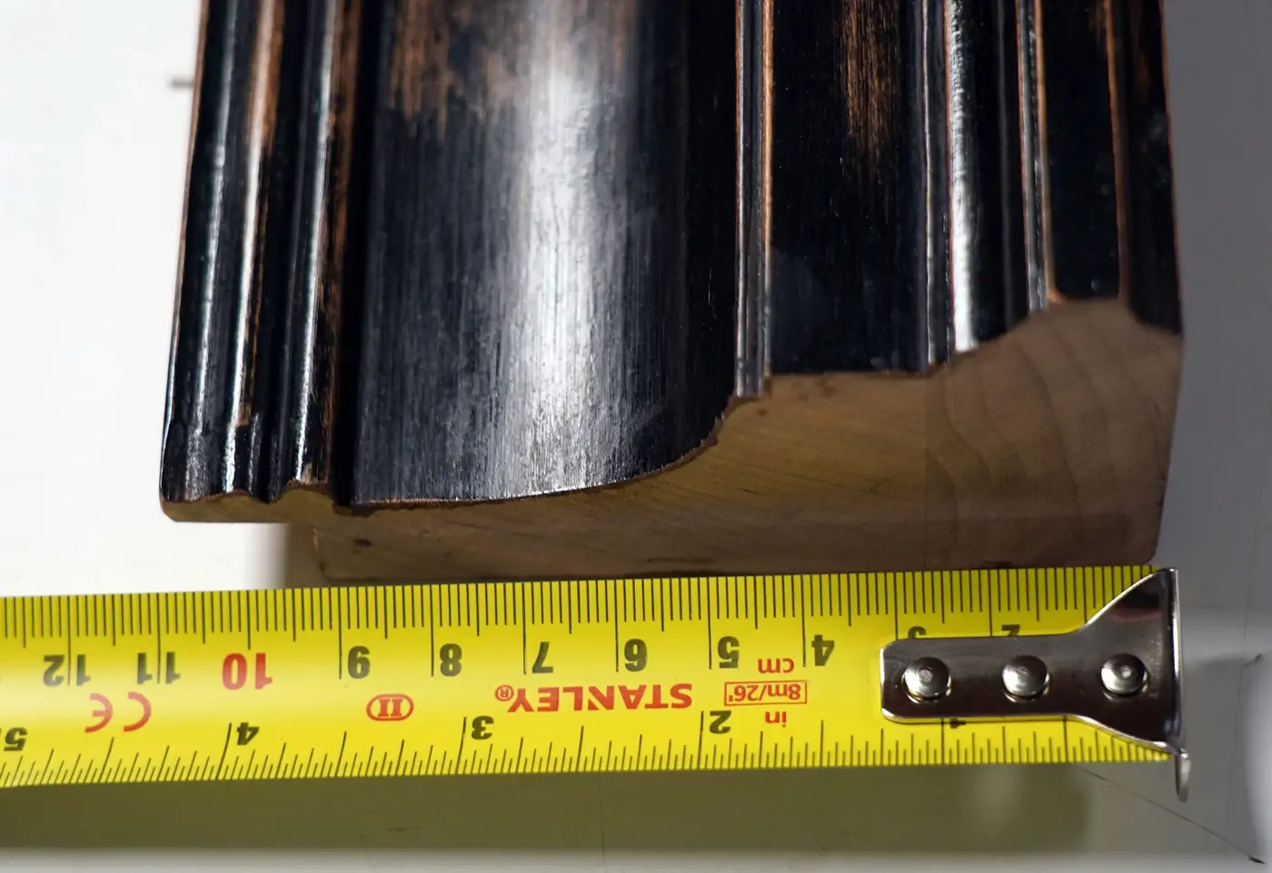 Corner detail of a hand-finished black lacquered frame profile beside its raw, unfinished wood