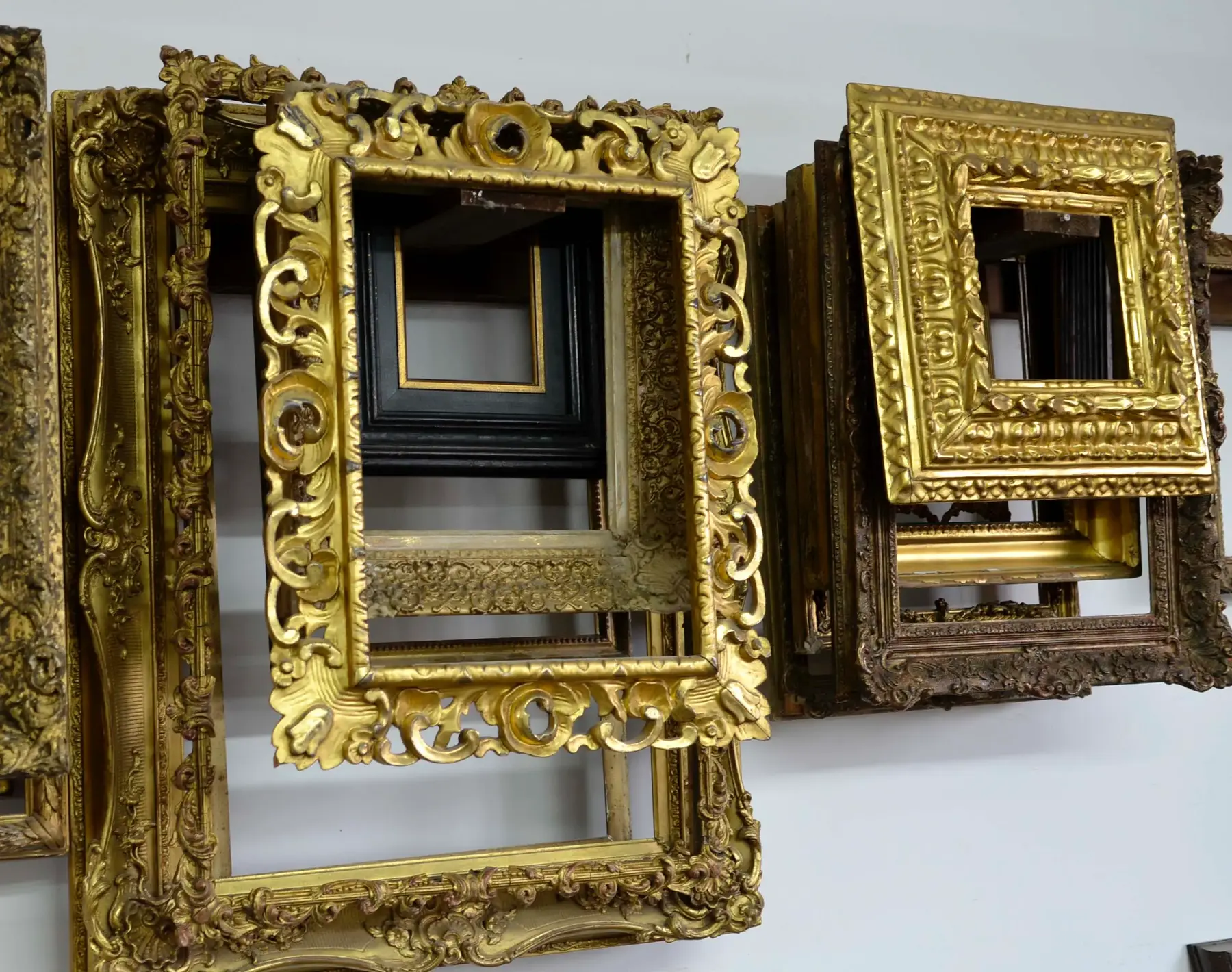 A wall of ornate hand-carved and gilded frames of varying styles and sizes, made entirely in our studio