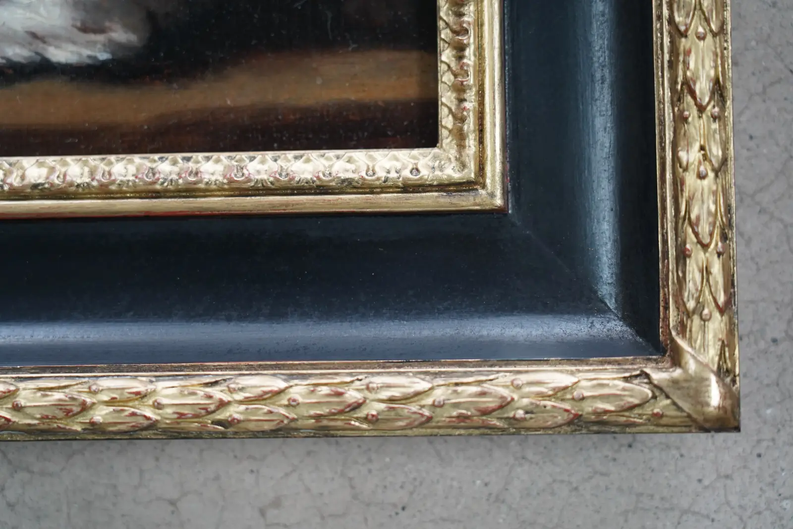 Corner of a period-style black and gold beaded frame surrounding a dark oil painting