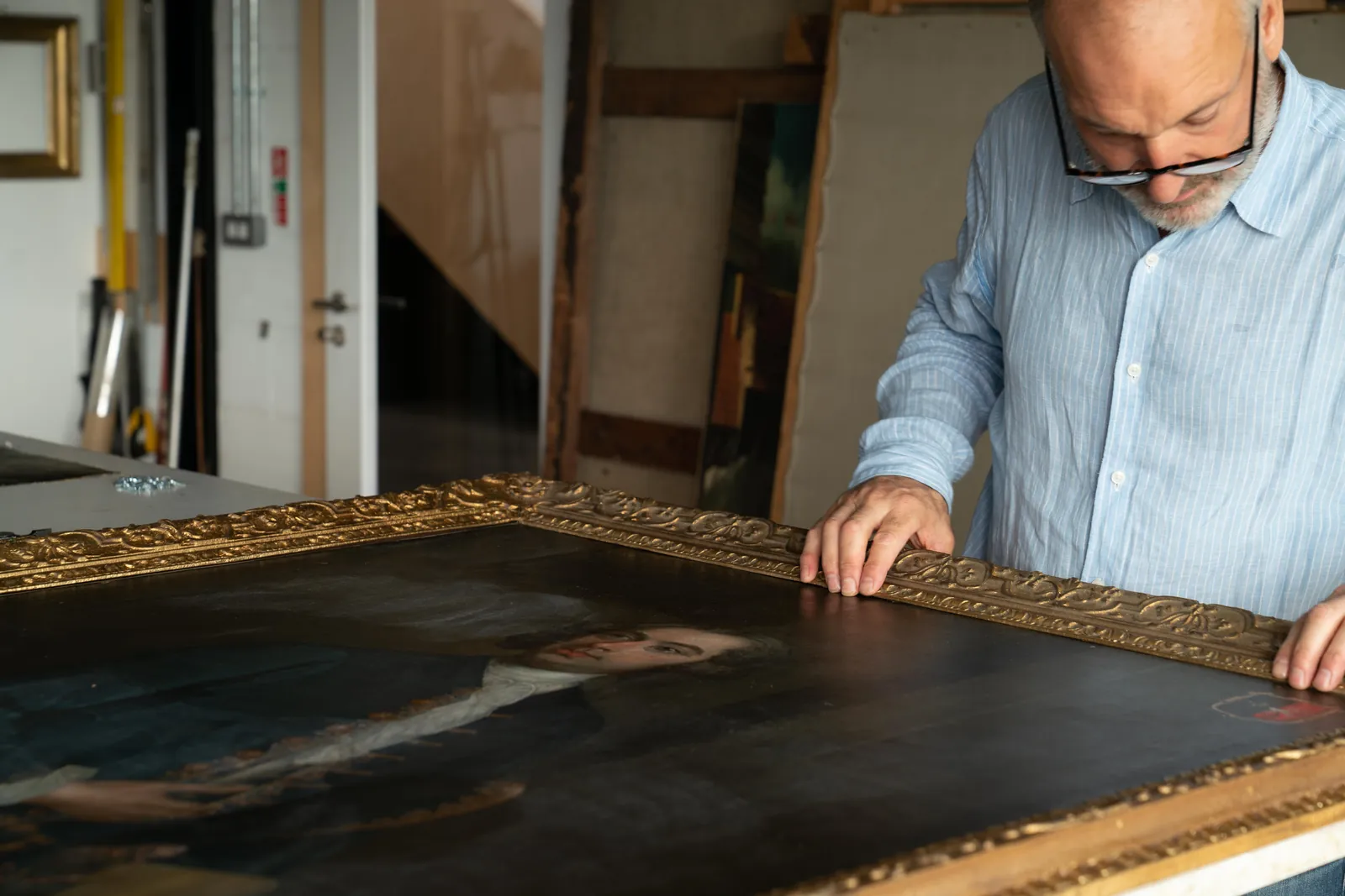 A conservator examining the gilt frame and canvas of a portrait painting in the Everett Fine Art studio